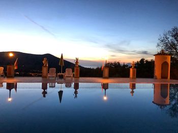 Reflection of trees in swimming pool against sky at sunset