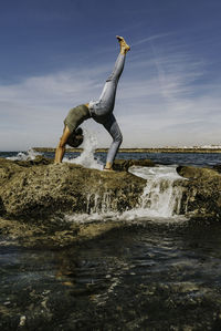 Man surfing on rock by sea against sky