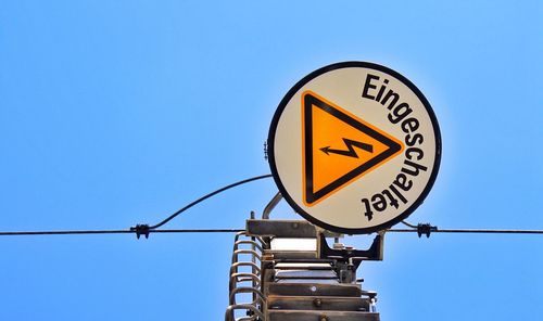 Low angle view of sign board against clear blue sky