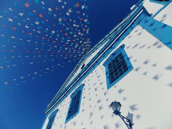 Low angle view of flags hanging on church against blue sky during sunny day