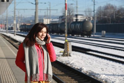 Smiling woman talking on phone while standing on railroad station platform