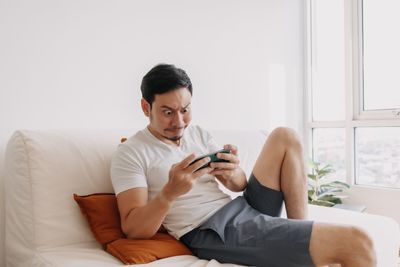 Young woman using mobile phone while sitting on bed at home