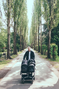 Father pushing baby carriage on road amidst trees