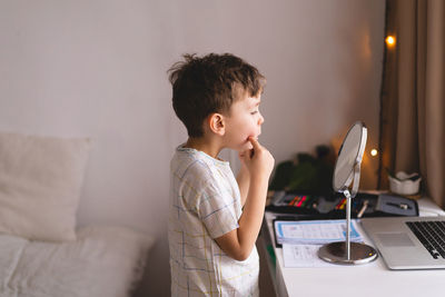 Boy pronouncing sound o looking at mirror doing an online speech therapy lesson through a laptop