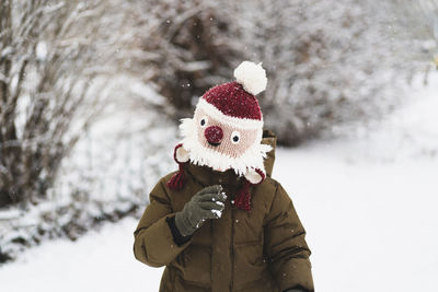 Cute little boy in funny winter hat walks during a snowfall. outdoors winter activities for kids.