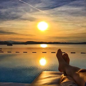 Low section of woman relaxing on sea shore against sunset sky