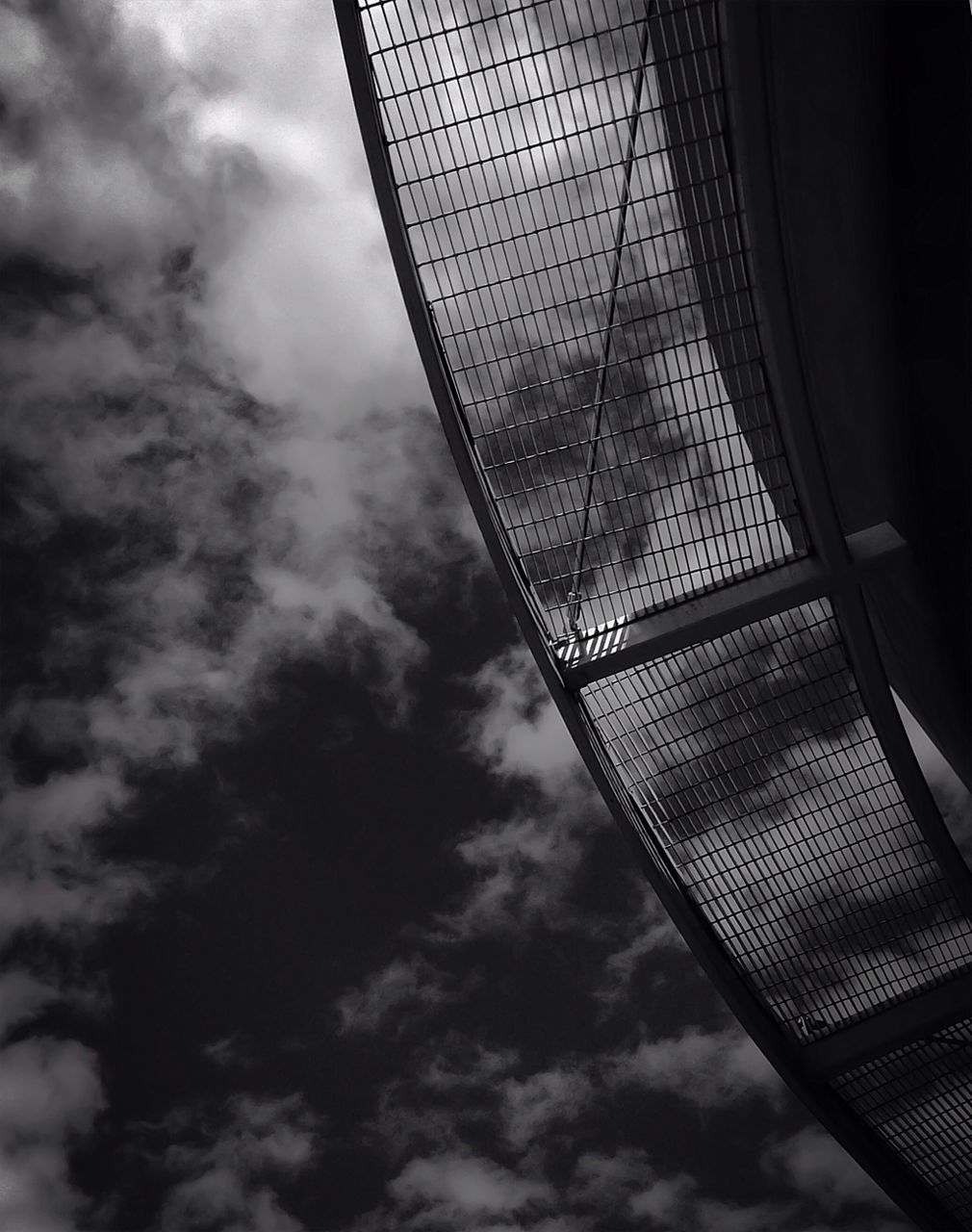 low angle view, sky, cloud - sky, cloudy, cloud, built structure, architecture, no people, glass - material, day, modern, metal, electricity, technology, outdoors, directly below, window, lighting equipment, part of, building exterior