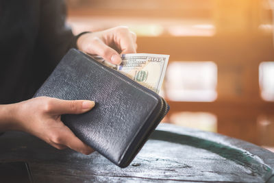 Cropped hands of woman removing paper currency from purse at table