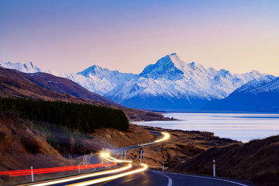 Light trails on road by mountains against clear sky at night