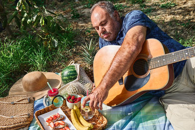 Middle aged couple having a picnic in the garden with fresh exotic fruit and sweet sandwiches.