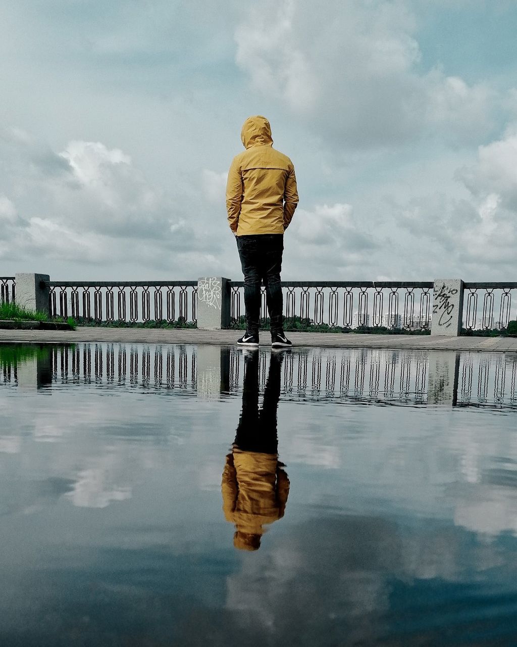 water, cloud, reflection, sky, one person, full length, nature, rear view, adult, architecture, footwear, day, lifestyles, casual clothing, clothing, built structure, bridge, rain, outdoors, winter, standing, railing, leisure activity, person, wet, women, sea, overcast, pier, environment