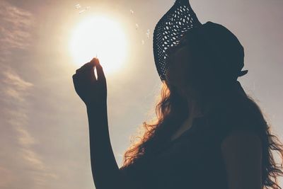 Optical illusion of woman blowing dandelion seeds against sun