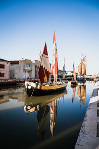 Sailboats moored in canal against clear sky