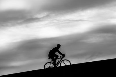 Silhouette man riding bicycle against sky