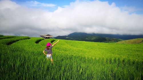 Rear view of woman in farm against cloudy sky