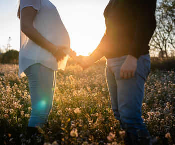 Midsection of couple standing on field against bright sun