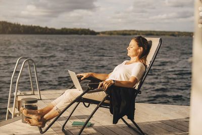 Full length of woman relaxing on deck chair at jetty over lake