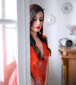 Portrait of young woman standing by window at home