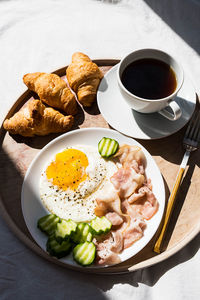 Breakfast in bed coffee cup, fried egg, bacon and croissants on wooden tray. 