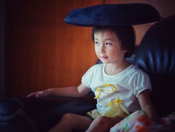 Cute girl balancing cushion on head while sitting at home