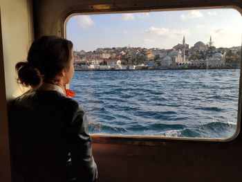 Rear view of woman standing by ferry window in city