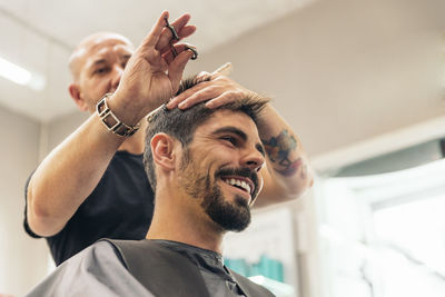 Low angle view of barber cutting man hair in salon