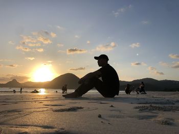 Side view of man standing at beach against sky during sunset