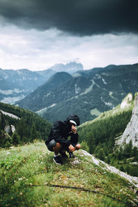 Man wearing hoodie crouching against mountain range