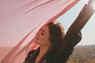 Young woman with pink scarf standing against sky during sunset