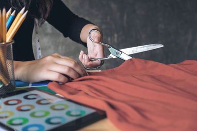 Cropped image of fashion designer cutting red fabric at desk