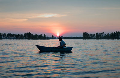 Man boating on sea against sky during sunset