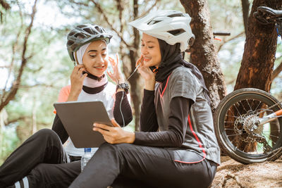 Friends using laptop while sitting on tree