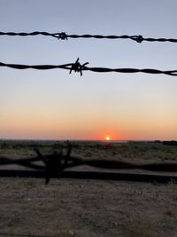 Silhouette of barbed wire against sky during sunset