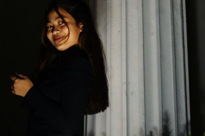 Portrait of smiling young woman standing against patterned wall at night