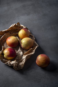 Paper weapped ripe peaches on dark surface