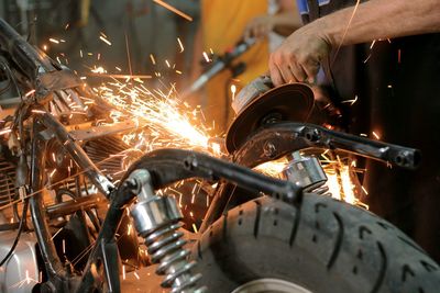 Cropped hand welding parts in motorcycle repair workshop