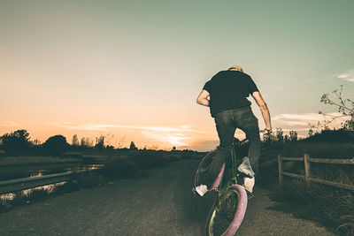 Rear view of man riding bicycle on road against sky