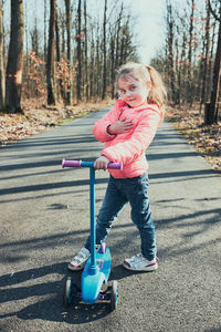 Portrait of cute girl by push scooter on road