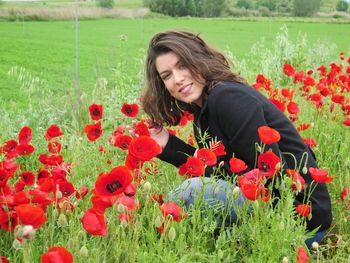 Portrait of smiling young woman with red poppy flowers in field