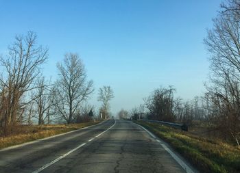 Empty road along bare trees against clear sky