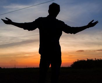 Silhouette man standing on field against sky during sunset