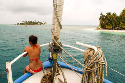 Rear view of woman wearing bikini sitting on boat in sea