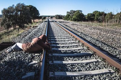 Person relaxing on railroad track against sky
