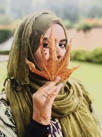 Close-up portrait of young woman in hijab holding leaf