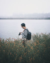 Side view of young man holding camera by lake