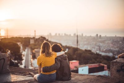 Rear view of couple looking at cityscape against sky during sunset