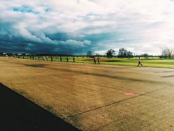 People on grassy field against cloudy sky