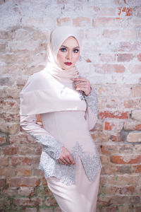 Portrait of young woman standing against brick wall