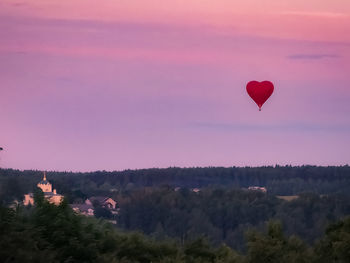 Hot air balloon flying over trees against sky during sunset