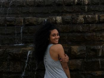 Rear view portrait of cheerful teenage girl standing against waterfall